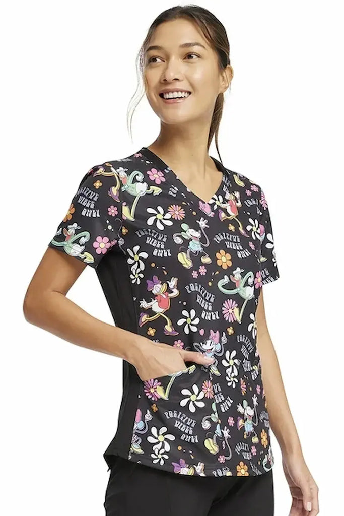 A young female Psychiatric Nurse wearing a Tooniforms Women's V-neck Printed Scrub Top in "Positive Vibes" size XS featuring a soft and breathable fabric made of 55% cotton and 45% polyester blend for exceptional comfort and long-lasting wear.