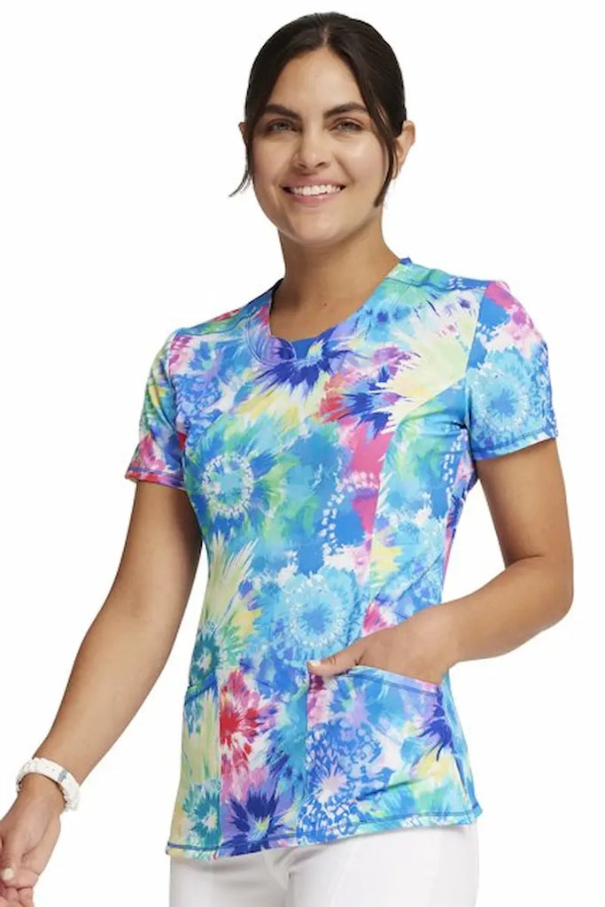 A young female Pediatric Nurse wearing a Cherokee Infinity Women's Round Neck Printed Scrub Top in size Medium featuring an eye-catching Tie-Dye Print.