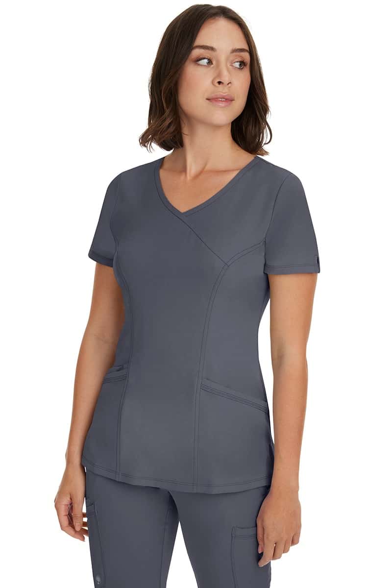 A young woman wearing a Women's Madison Mock Wrap Scrub Top from HH Works in Pewter featuring a medium center back length of 24".