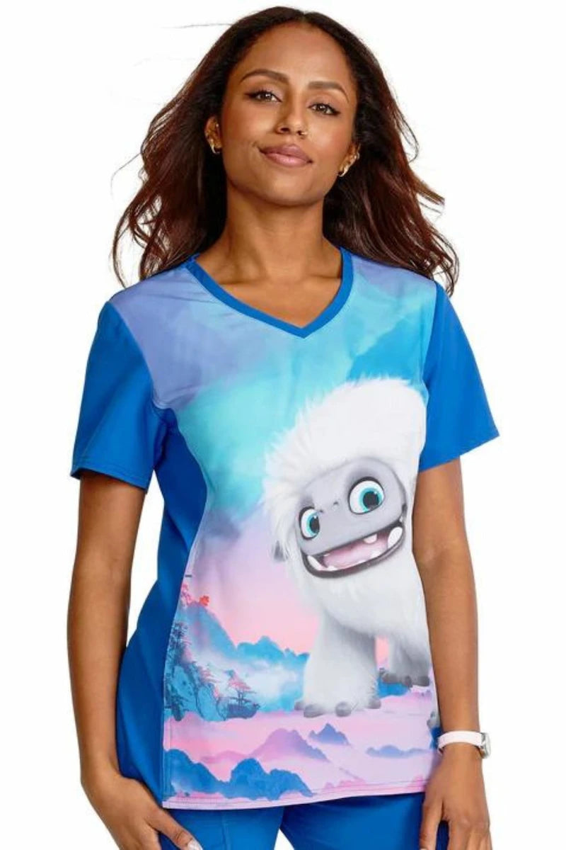 A young female children's nurse displaying the front of the "Abominable Snowman" Tooniforms Women's V-Neck Print Scrub Top on a white background.