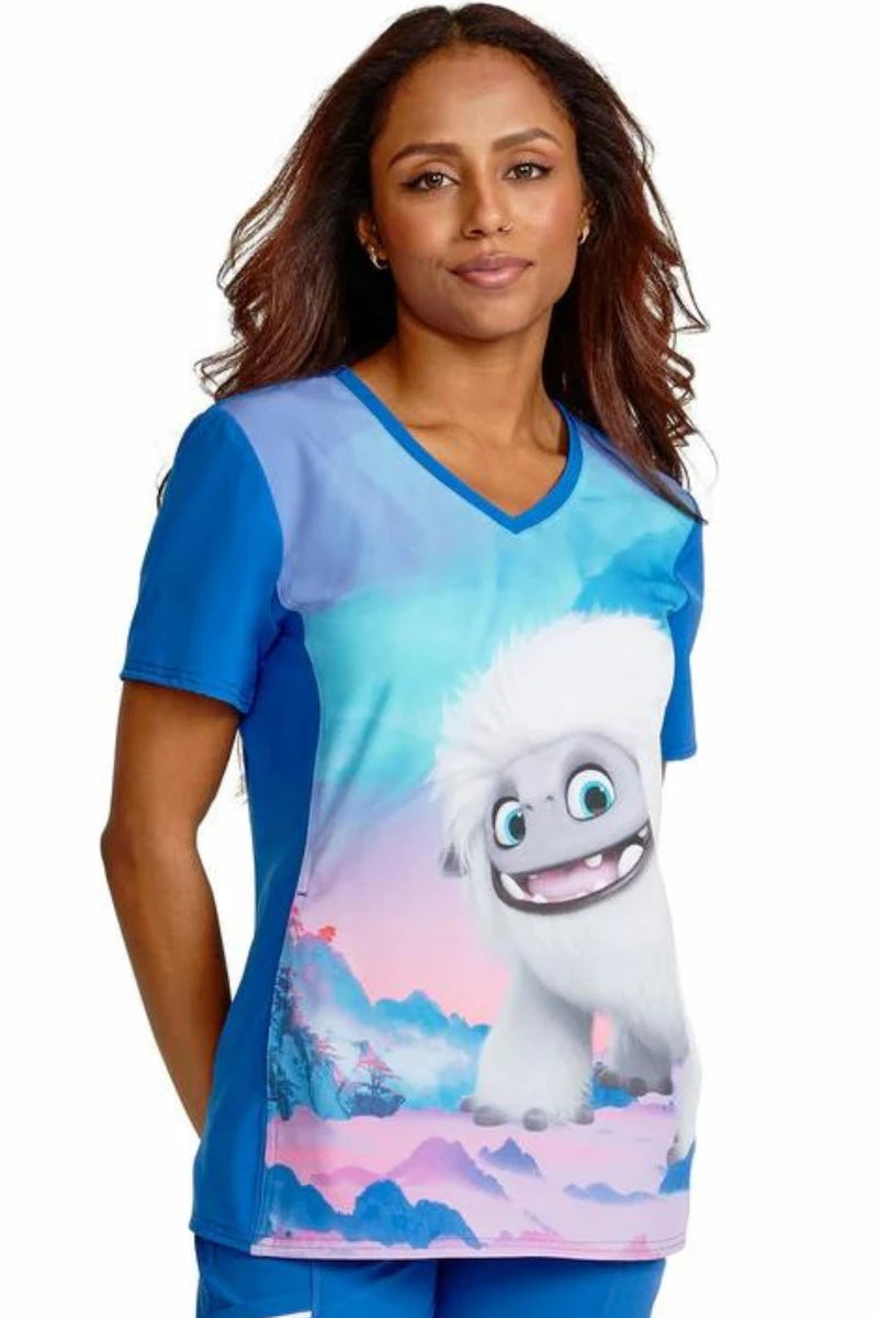 A young female Pediatric Nurse displaying the right side of the Tooniforms Women's V-Neck Print Scrub Top in Abominable Snowman featuring back vents and solid knit side panels.