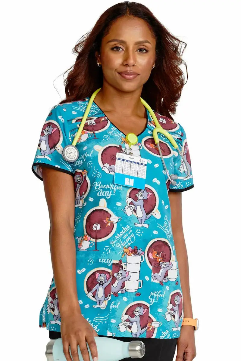 A young female Children's Nurse wearing a Tom and Jerry themed print scrub top from Cherokee Tooniforms on a white background.