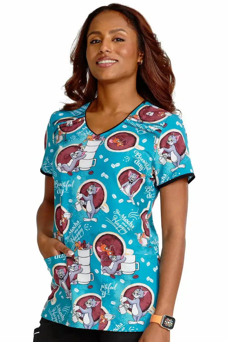 A young female nurse displaying the left side of the Tooniforms Women's V-Neck Print Scrub Top in Mocha Me Happy featuring two front patch pockets.