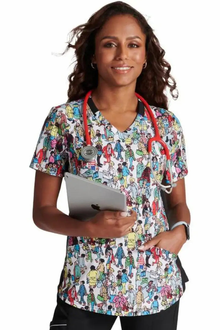 A young female Pediatric Nurse showcasing the front of the "Where's Waldo" Tooniforms Women's V-Neck Print Scrub Top in size Small.