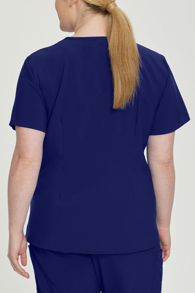 A young female Nursing Assistant showcasing the back of the urbane Performance Women's Motivate V-neck Scrub Top in True Navy size 4XL featuring a modern, tailored fit.