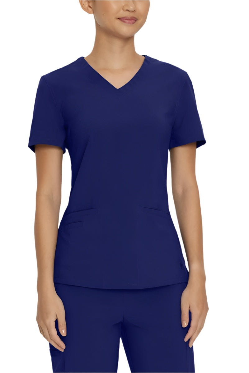 A young female LPN wearing an Urbane Performance Women's Motivate V-neck Scrub Top in True Navy size XS featuring a unique, 4-way stretch fabric.