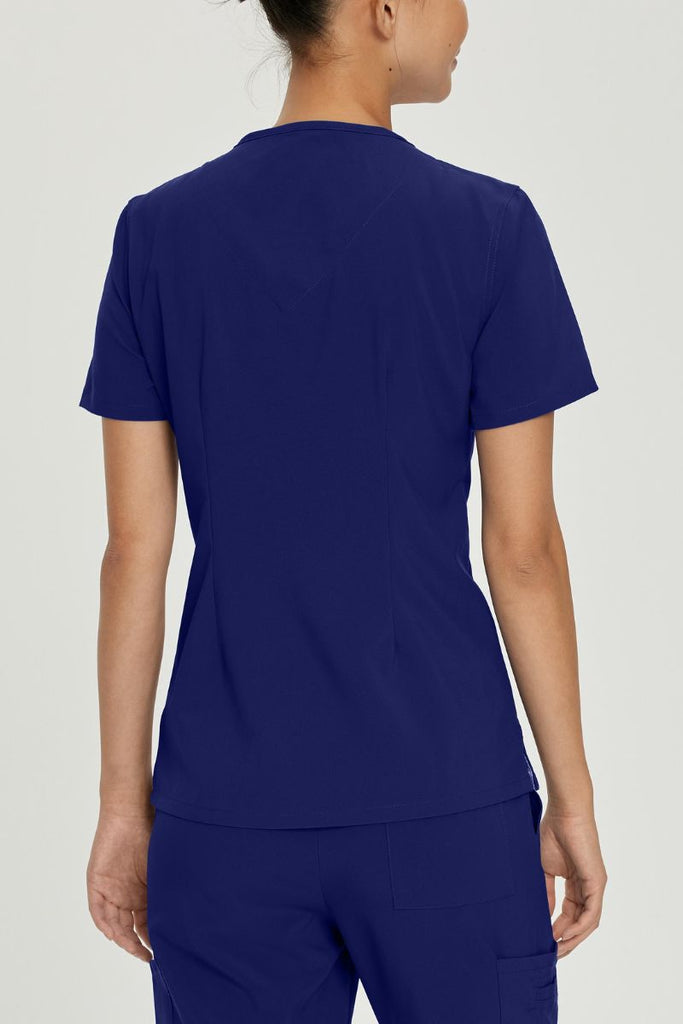 A young female LVN wearing an Urbane Performance Women's Motivate V-neck Scrub Top in True Navy size Medium featuring a center back length of 26.5"