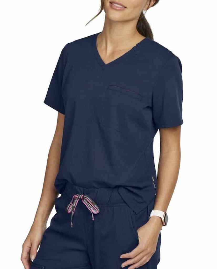 An image of a young female Nurse Practitioner wearing a Vince Camuto Women's Tuckable V-neck Scrub Top in Navy size Medium featuring a contemporary fit.