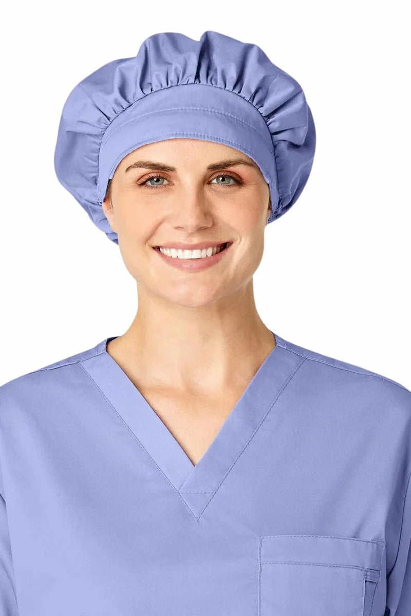 A young female Surgical Assistant wearing a WonderWink Women's Bouffant Scrub Cap in Ceil Blue made from a soft, breathable fabric.