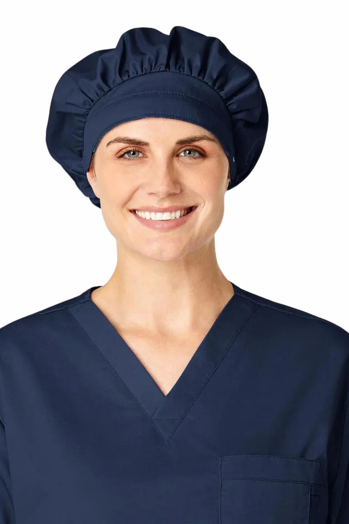 A young female Medical Assistant displaying the WonderWink Women's Bouffant Scrub Cap in Navy Blue featuring a sweat-absorbing terry band.