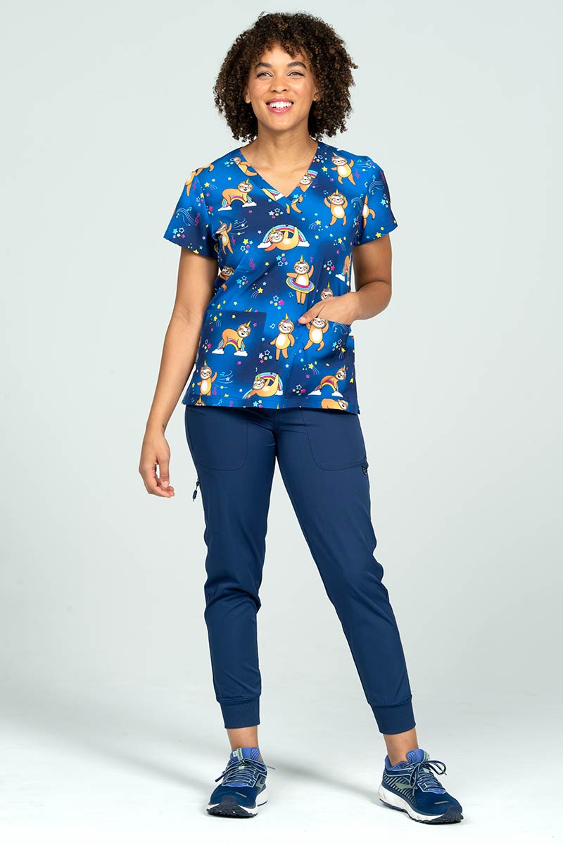 A full body picture of a young female RN wearing a Meraki Sport Print Scrub Top in "Sloth Squad" size Medium featuring shoulder yokes for shaping.