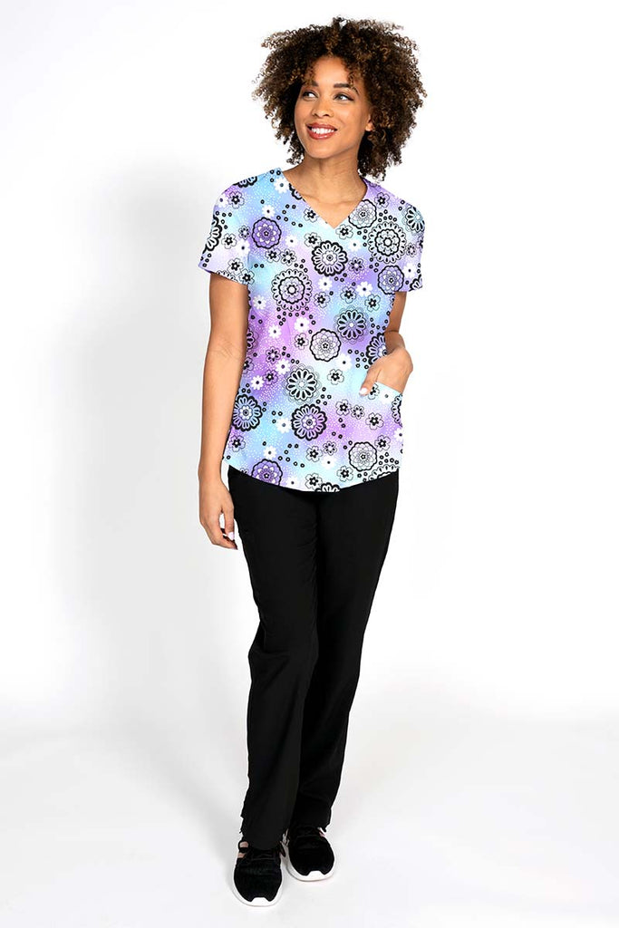 A young female LPN wearing the Meraki Sport Women's Print Scrub Top in "Lovely Lavender featuring 2 front patch pockets.