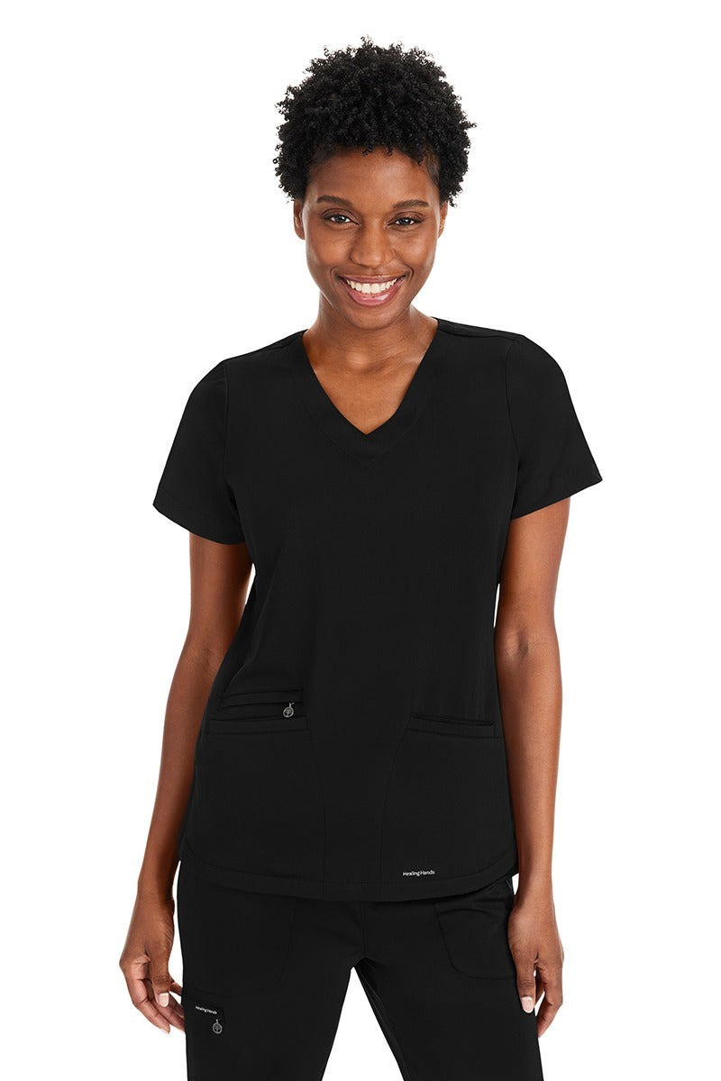A young female Nurse Practitioner wearing a Purple Label Women's Andes Curved V-Neck Scrub Top in "Black" size Medium featuring 2 front patch pockets.