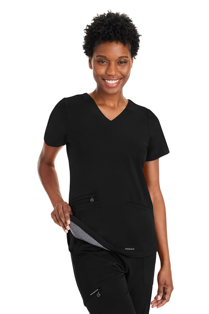 A young female Pharmacy Technician wearing an Andes Curved V-Neck Scrub Top from Purple Label by Healing Hands in "Black" size XS featuring an added layer of knit fabric throughout.