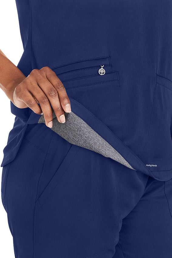 A young female Dental Hygienist wearing a  Purple Label Women's Andes Curved V-Neck Scrub Top in "Navy" size Large featuring 1 zipper close pocket on the wearer's front right side. 
