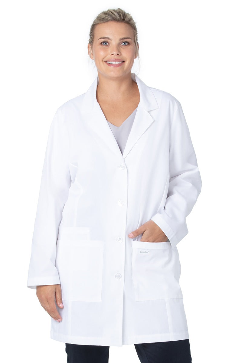 A young female Doctor wearing a Landau Women's 3-Pocket Button Front Lab Coat  in White Sanded size XXS featuring a four button front closure.