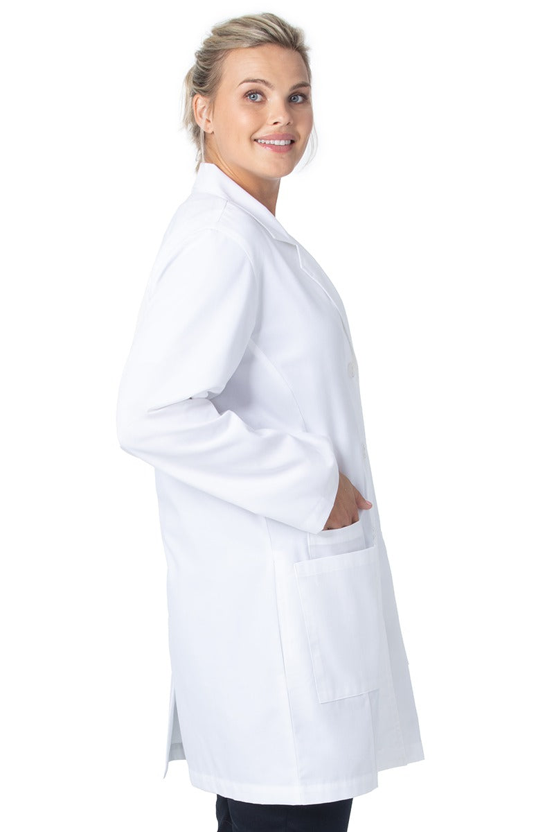 A young female Lab Technician wearing a Landau Women's 3-Pocket Button Front Lab Coat in White Sanded size Small featuring 2 front patch pockets with an accessory pocket on the wearer's right side.