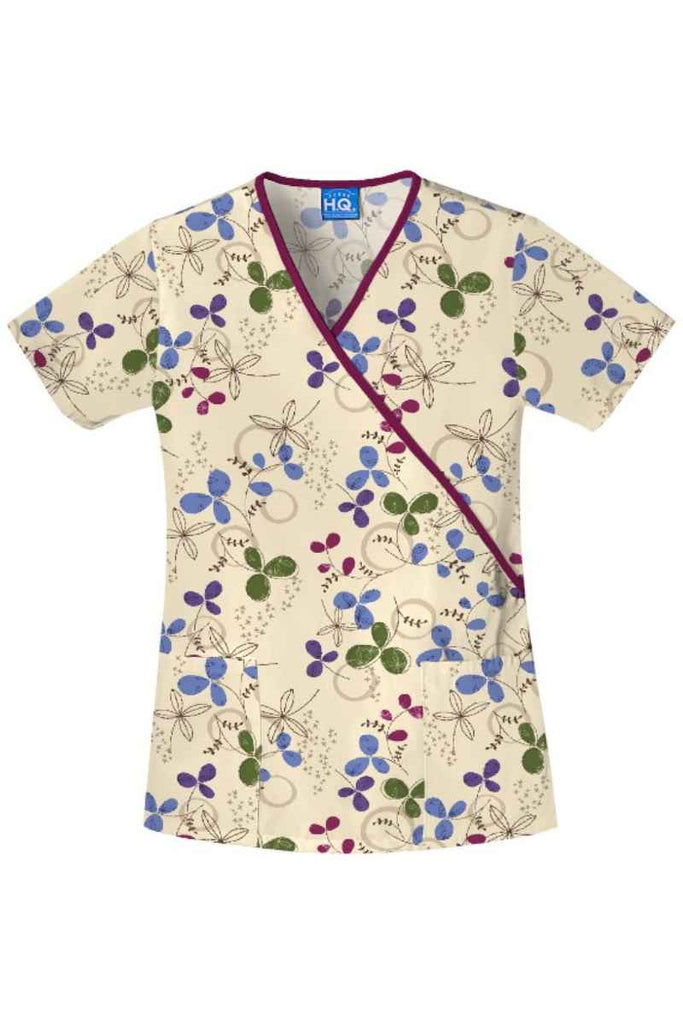 A frontward facing image of the Cherokee Women's Mock Wrap Scrub Top in "Clover Park" feturing  a geometric floral print in beautiful purple and green tones.