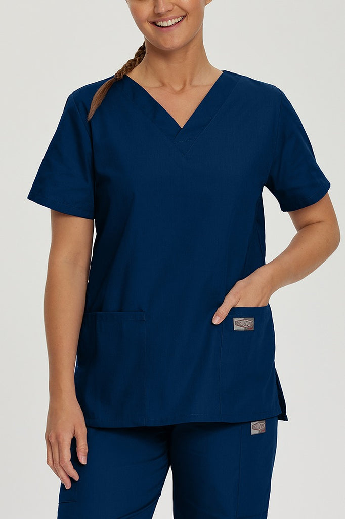 A young female Medical Assistant wearing a Landau ScrubZone Women's V-Neck Scrub Top in True Navy size Medium featuring a generous fit complemented by side vents for extra movement and all-day wearability.