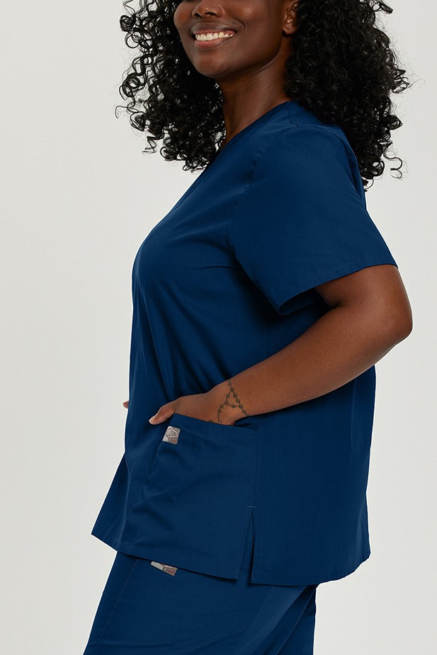 A female Nurse Practitioner wearing a Landau ScrubZone Women's V-neck Scrub Top in True Navy size 5XL featuring side vents for additional ease of movement.