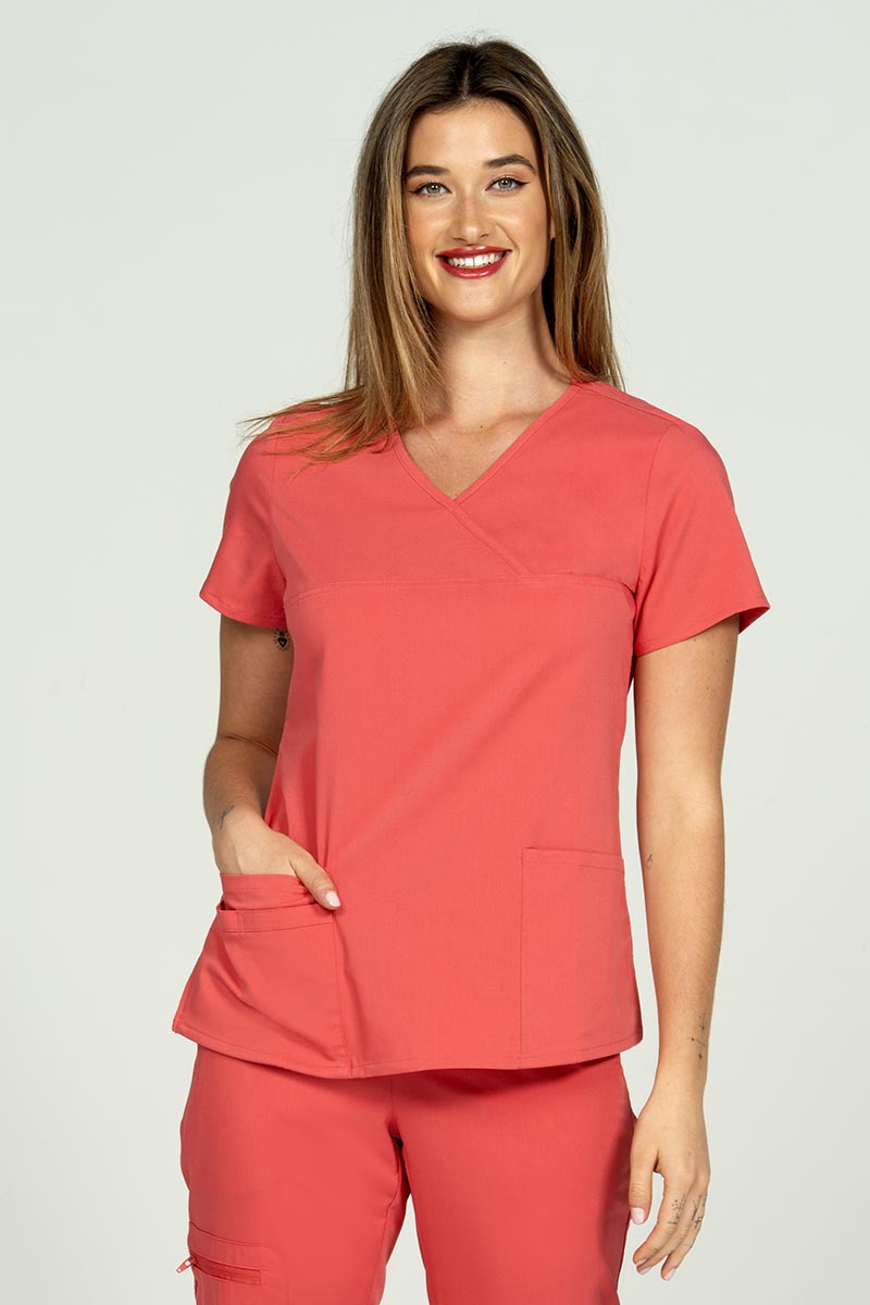 A young female LPN wearing an Epic by MedWorks Women's Y-Neck Scrub Top in Coral featuring a Y-neckline with short sleeves.