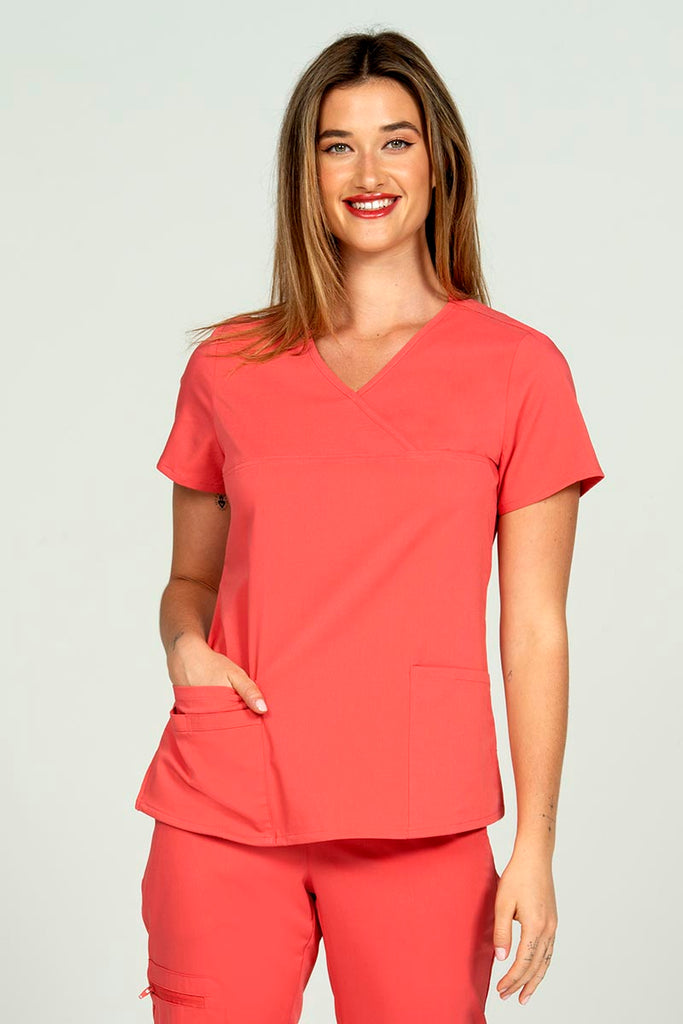A young female LPN wearing an Epic by MedWorks Women's Y-Neck Scrub Top in Coral featuring a Y-neckline with short sleeves.
