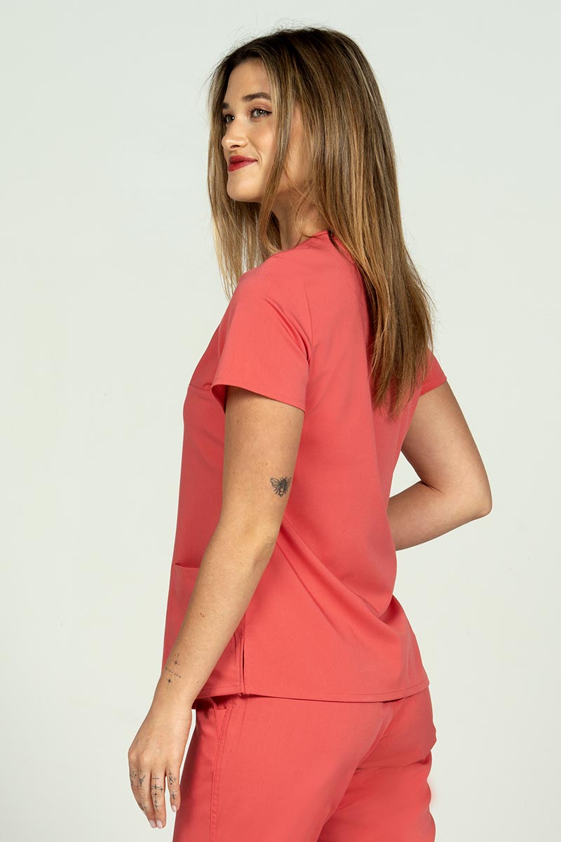 A female Home care Registered Nurse wearing an Epic by MedWorks Women's Y-Neck Scrub Top in Coral size medium featuring side slits at the hem.