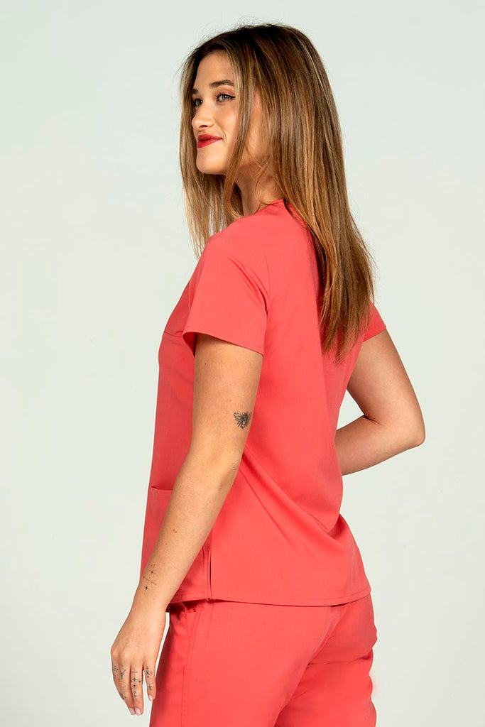 A female Home care Registered Nurse wearing an Epic by MedWorks Women's Y-Neck Scrub Top in Coral size medium featuring side slits at the hem.
