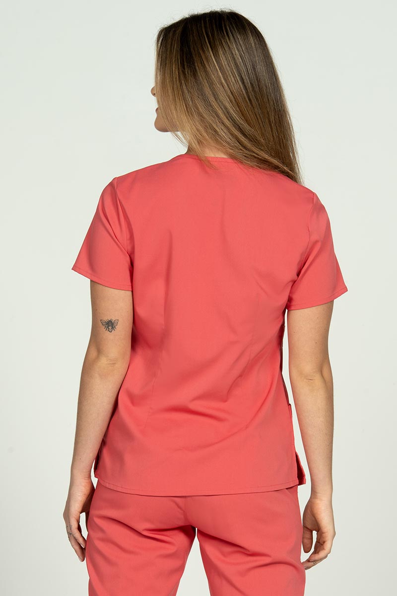 A young RN wearing an Epic by MedWorks Women's Mock Wrap Scrub Top in Coral featuring a tapered cut for a tailored look without losing mobility.