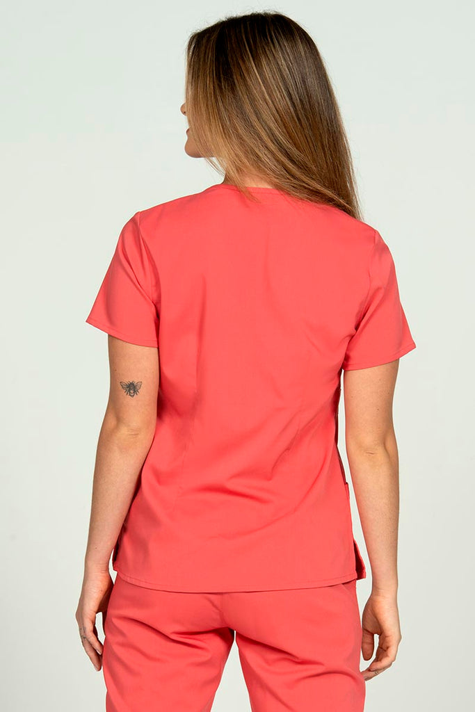 A young RN wearing an Epic by MedWorks Women's Mock Wrap Scrub Top in Coral featuring a tapered cut for a tailored look without losing mobility.