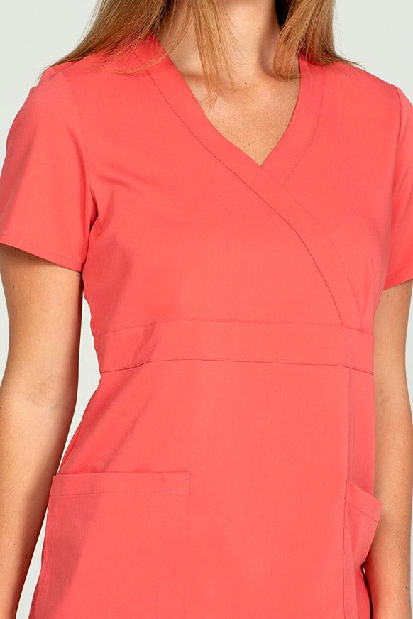 A young female healthcare worker wearing an Epic by MedWorks Women's Mock Wrap Scrub Top in Coral size XL featuring a stylish mock wrap neckline.