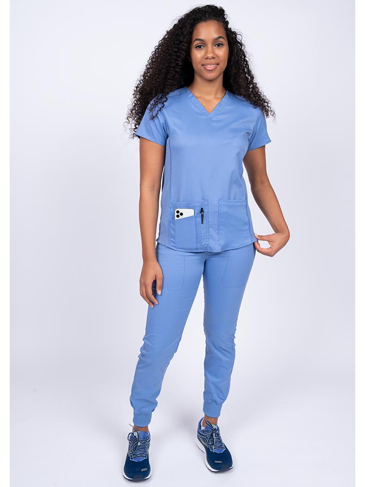 Young female healthcare professional wearing an Epic by MedWorks Women's Blessed Scrub Top in ceil with a total of 3 pockets & 1 pen slot.