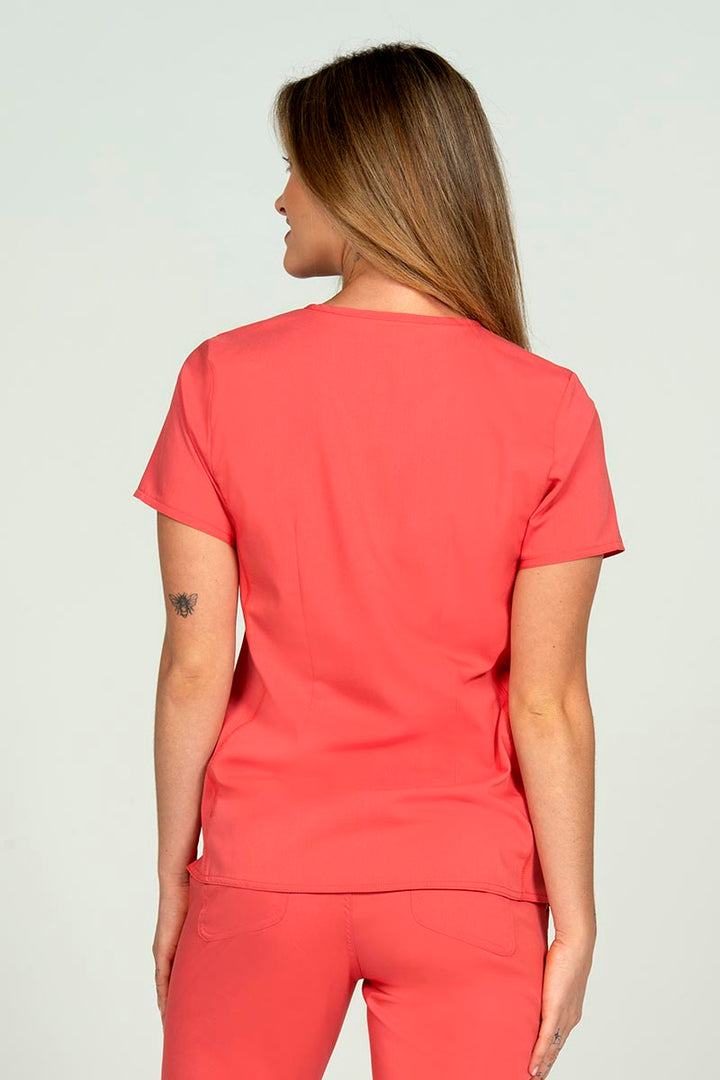 A female Nursing Assistant wearing an Epic by MedWorks Blessed Scrub Top in Coral size medium featuring a center back length of 26.5".