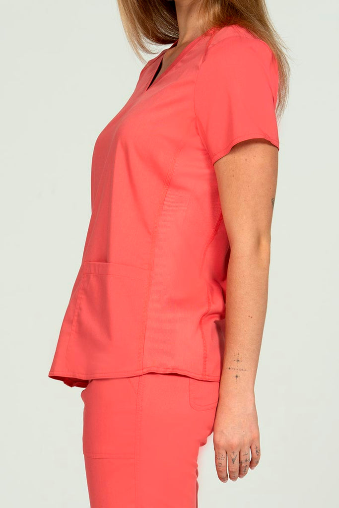 A female Nurse Practitioner wearing an Epic by MedWorks Women's Blessed Scrub Top in Coral size small featuring side stretch panels to ensure a comfortable fit while moving.