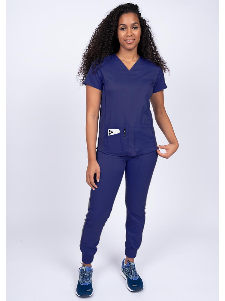 Young female healthcare professional wearing an Epic by MedWorks Women's Blessed Scrub Top in navy with a total of 3 pockets & 1 pen slot.
