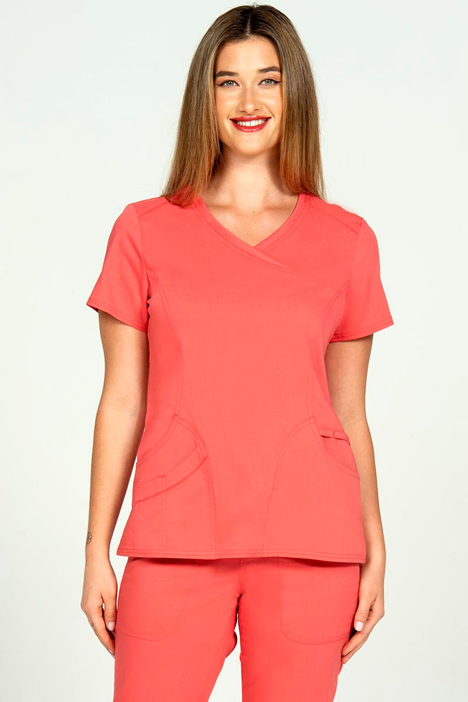 A young female Phlebotomist wearing an Epic by MedWorks Women's Knit Collar Mock Wrap Scrub Top in Coral size small featuring a y-neckline & short sleeves.