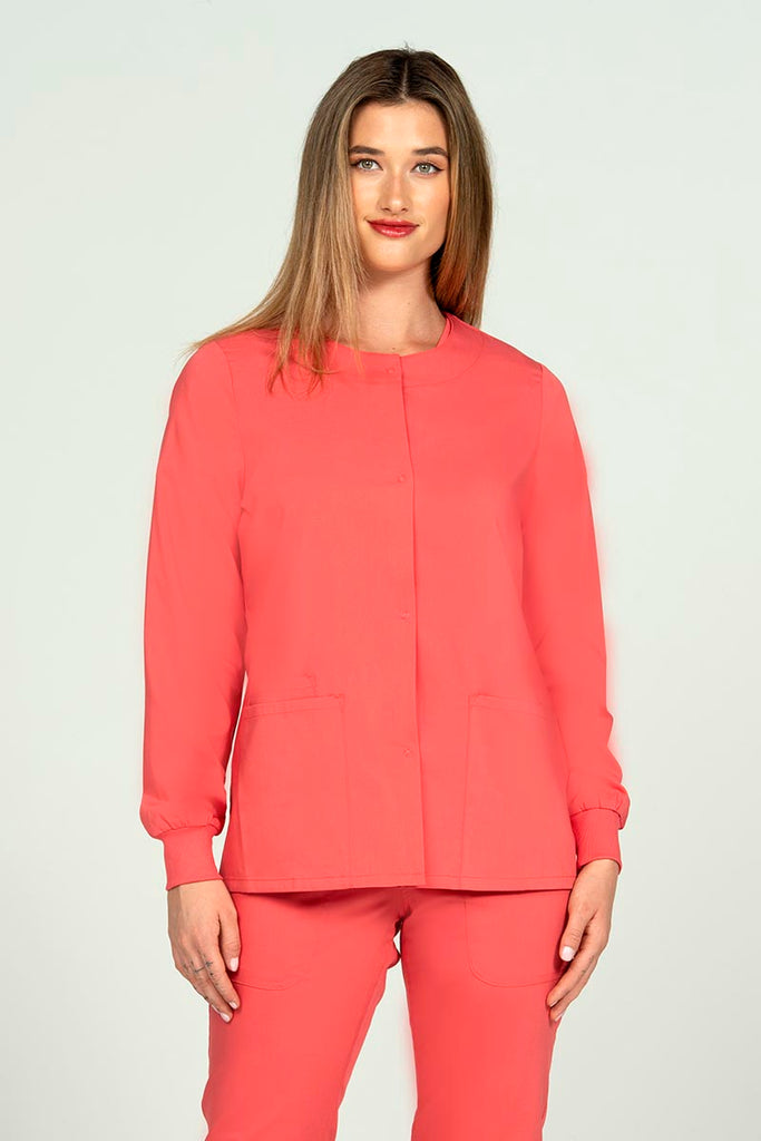 A young female healthcare worker wearing an Epic by MedWorks Women's Snap Front Scrub Jacket in Coral featuring snap front closure.
