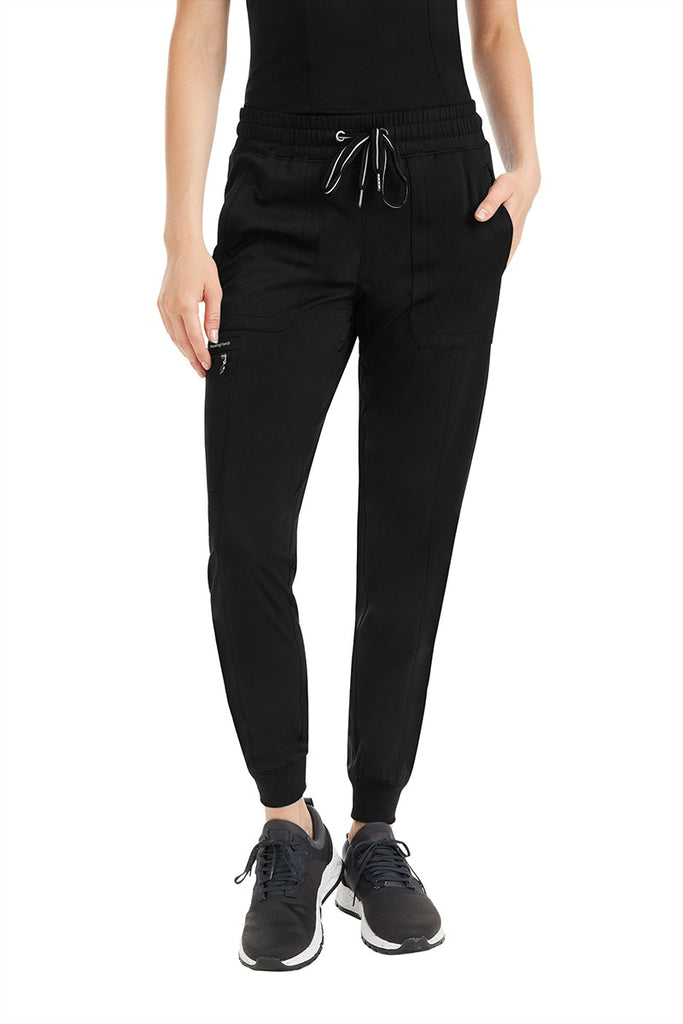 A female nurse practitioner wearing a pair of Women's Aspen Jogger Scrub Pant from Purple Label by Healing Hands in "Black" size Large Petite featuring a zip closure cargo pocket in the wearer's right side pant leg.