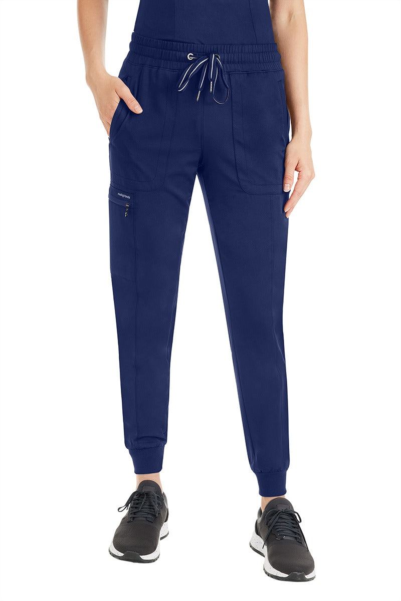 A female Nursing Assistant wearing a pair of  Women's Aspen Jogger Scrub Pants from Purple Label by Healing Hands in "Navy" size Medium Petite featuring a 2x2 rib knit waistband & leg cuffs.