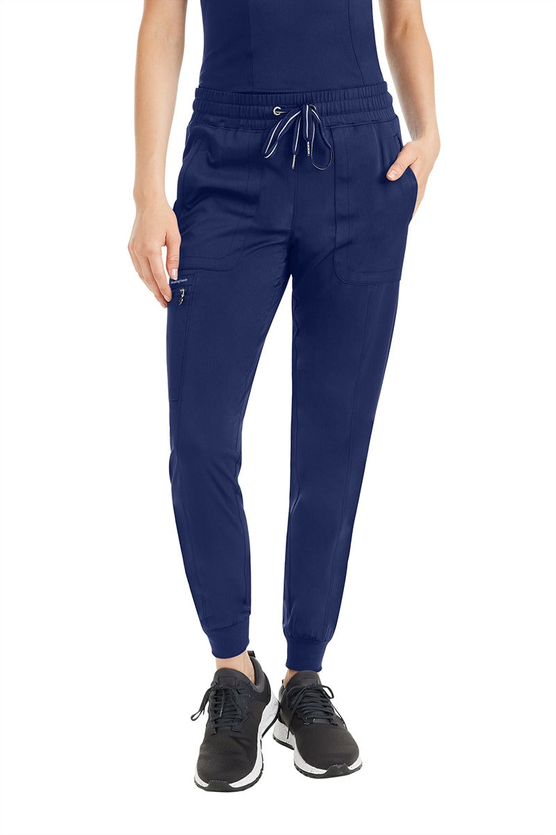 A female nurse practitioner wearing a pair of Women's Aspen Jogger Scrub Pant from Purple Label by Healing Hands in "Navy" size 2XL featuring a zip closure cargo pocket in the wearer's right side pant leg.