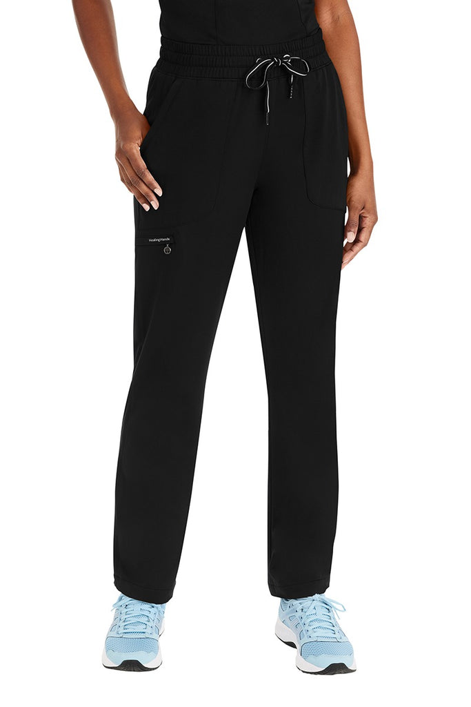 A young female Licensed Practical Nurse wearing a Purple Label Women's Knit Lined Alaskan Pant in "Black" size Medium Petite featuring 1 zip closure cargo pocket on the wearer's right side.