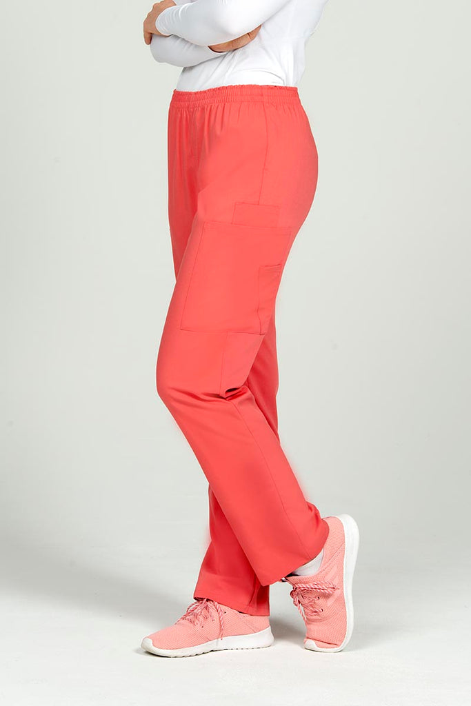 A young female Nurse Practitioner wearing an Epic by MedWorks Women's Elastic Waist Scrub pant in Coral size Medium featuring1 cellphone pocket on the wearer's left side.