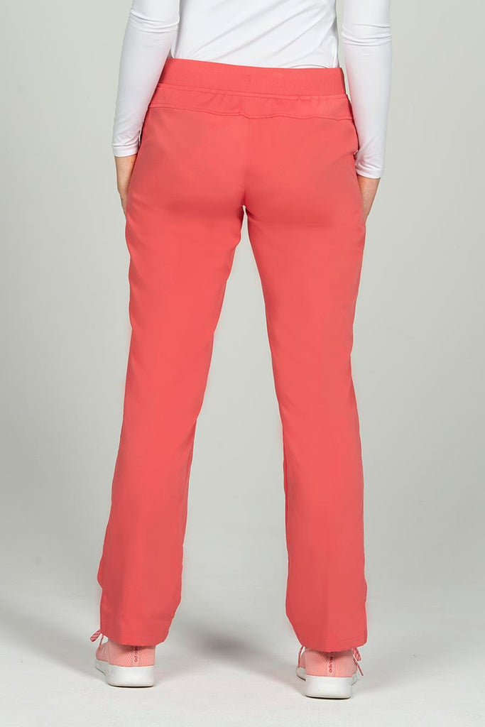 A young female Physician Assistant wearing an Epic by MedWorks Women's Skinny Yoga Scrub pant in Coral size XS Petite featuring a unique stretch fabric made of 77% Polyester, 21% Viscose, 2% Spandex.