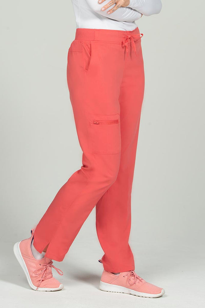 A female Nurse Practitioner wearing an Epic by MedWorks Women's Skinny Yoga Scrub Pant in Coral size XS featuring side slits.