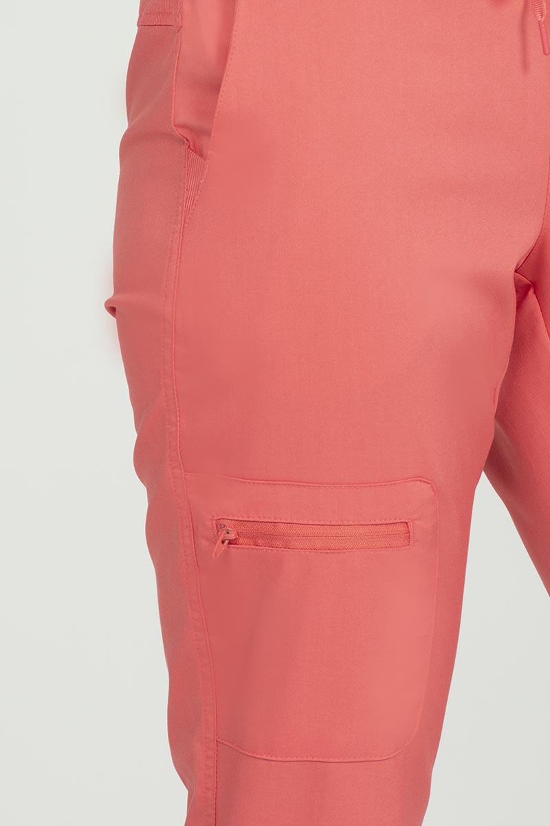 A young female Nurse wearing an Epic by MedWorks Women's Skinny Yoga Scrub Pant in Coral size 2XL featuring 1 zip closure cargo pocket on the wearer's right side.