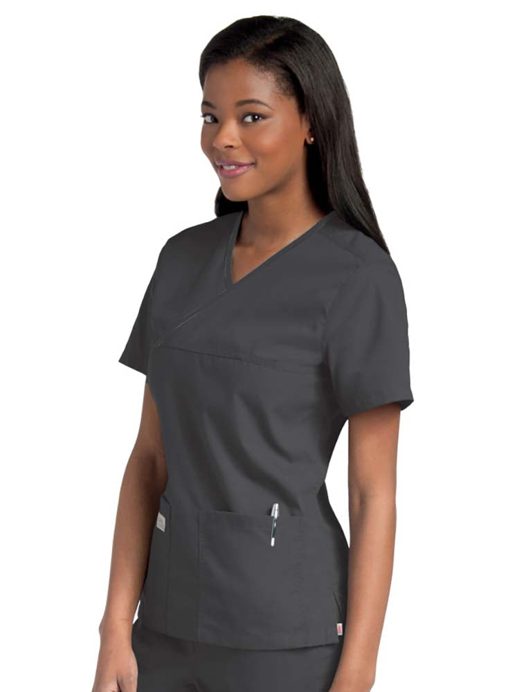 Female nurse wearing an Urbane Essentials Women's Crossover Scrub Top in "Black" featuring 2 front patch pockets.