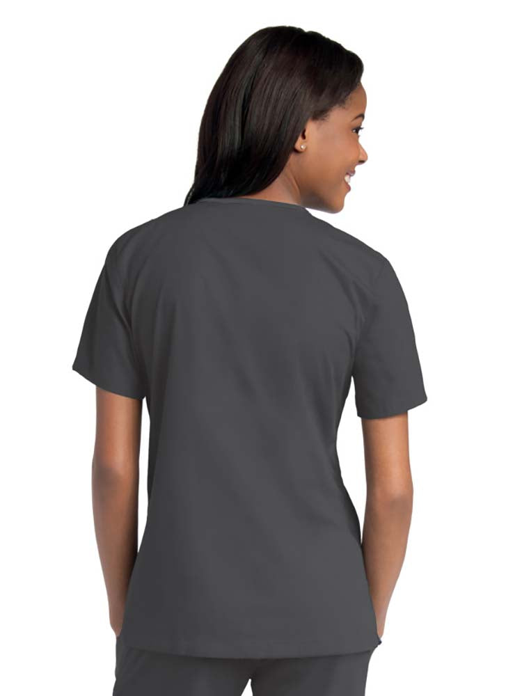 Young female healthcare worker wearing an Urbane Essentials Women's Crossover Scrub Top in "Black" featuring side vents for increased range of motion.