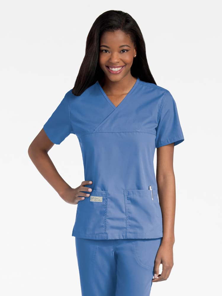 Young lady wearing an Urbane Essentials Women's Crossover Scrub Top in "Ceil" featuring a unique crossover neckline for a flattering fit.