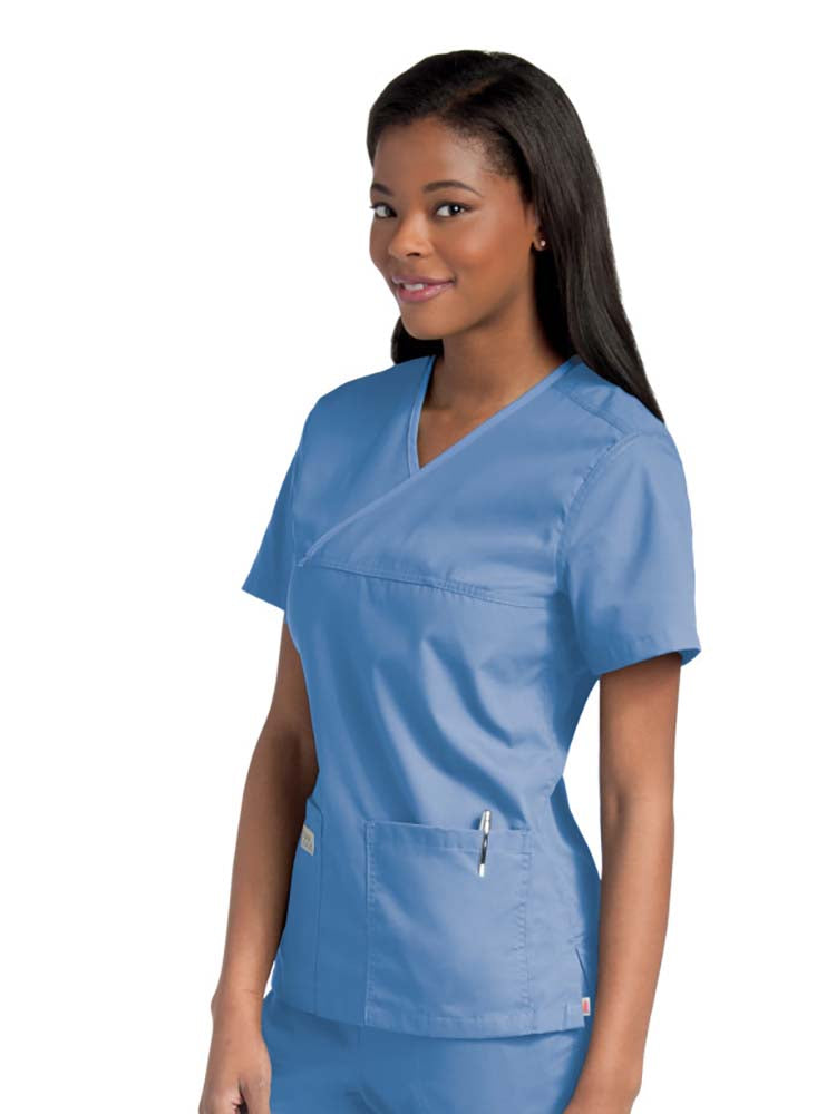 Female nurse wearing an Urbane Essentials Women's Crossover Scrub Top in "Ceil" featuring 2 front patch pockets.