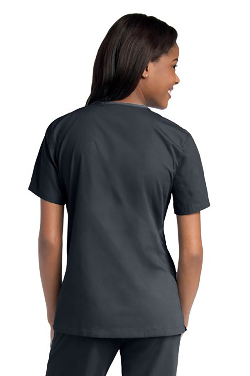 Young female healthcare worker wearing an Urbane Essentials Women's Crossover Scrub Top in "Graphite" featuring side vents for increased range of motion.